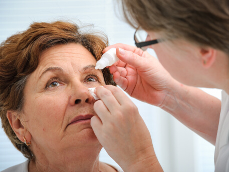 eye doctor putting eye drops in older female patient